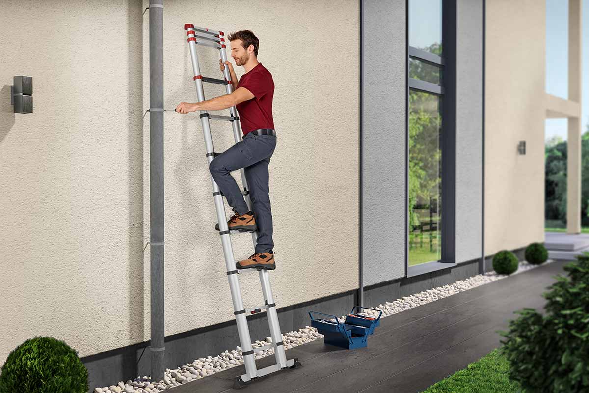 A man using a telescopic ladder to reach an area of his gutter.