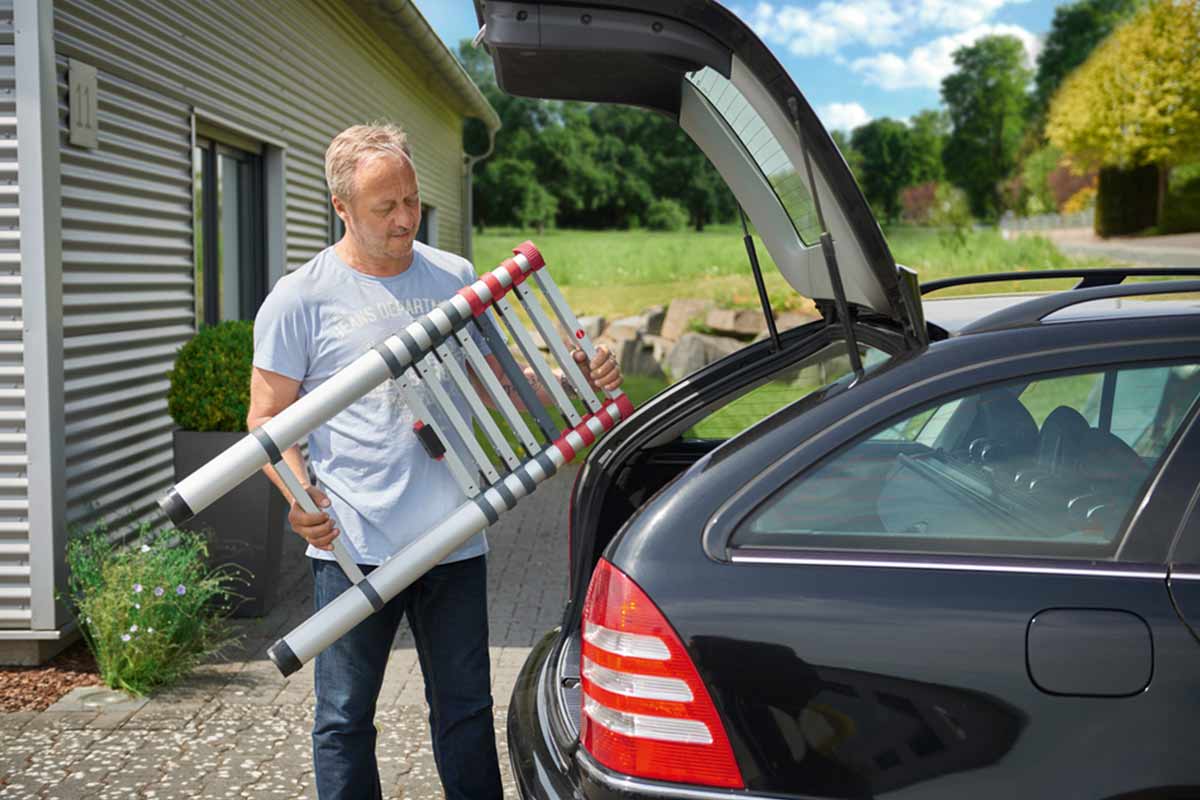A man loads his telescopic ladder into the boot of his car on a sunny day.